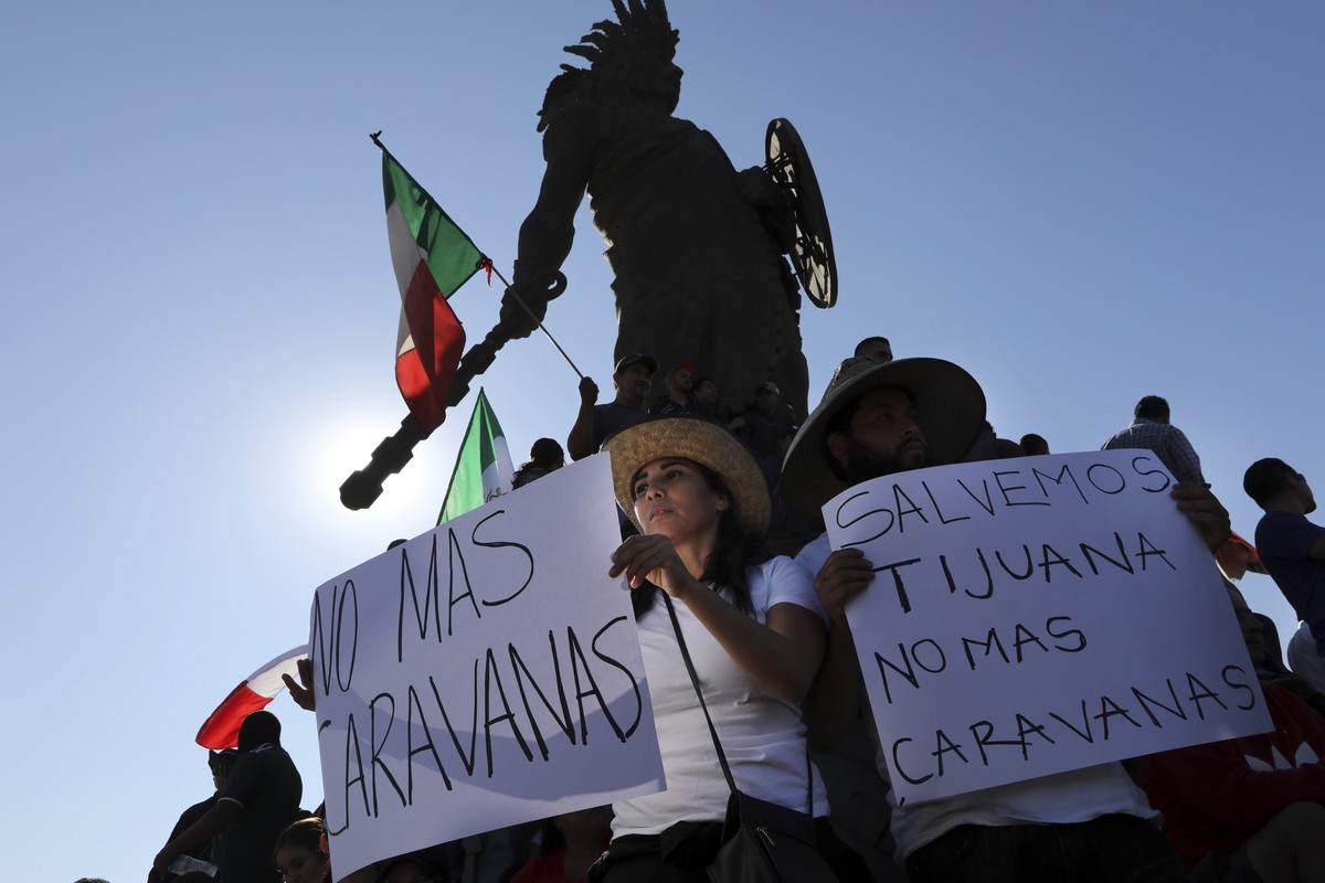 Demonstrators with signs that read in Spanish: "No more Caravans", and "Let's save Tijuana, no more caravans," stand under an statue of indigenous Aztec ruler Cuauhtemoc to pr ...