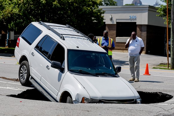 epa10714393 Tow truck operators investigate the scene after an SUV was partially swallowed by a sinkhole along busy Ponce de Leon Avenue in downtown Atlanta, Georgia, U.S., June 27, 2023. Officials…