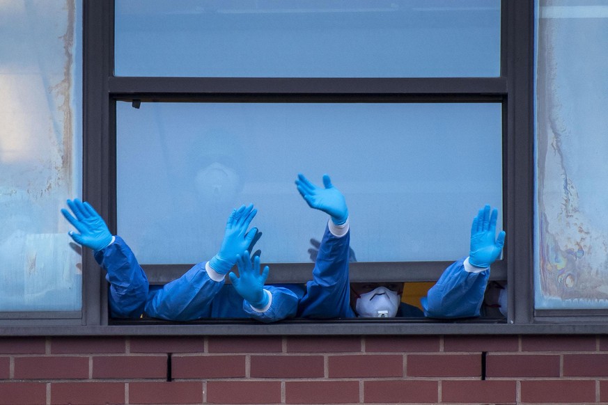 NEWPORT, UNITED KINGDOM - APRIL 23: Health workers wearing PPE clap from a window at the Royal Gwent Hospital on April 23, 2020 in Newport, United Kingdom. Following the success of the "Clap for ...