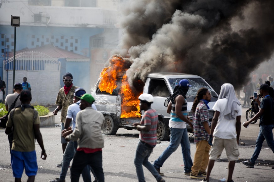 Smoke billows from a van set fire by protesters during clashes with police amid a protest demanding the resignation of Haitian President Jovenel Moise near the presidential palace in Port-au-Prince, H ...