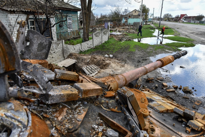 epa09913408 People walk near a destroyed tank in Kolychivka village, Chernihiv region, 27 April 2022. On 24 February, Russian troops entered Ukrainian territory in what the Russian president declared  ...