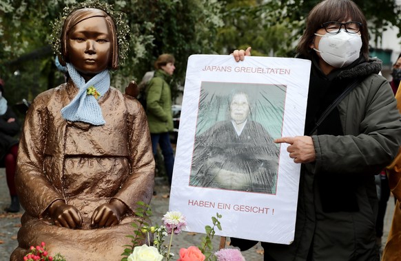 epa08740041 A woman holds a portrait of a former sex slave Park Young Sim during a demonstration where the Statue of Peace is located in Berlin, Germany, 13 October 2020. The Statue of Peace that was  ...