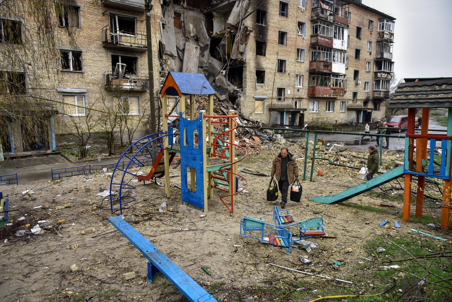 epa09991176 (FILE) - People carry bags at a playground of a damaged apartment block in Horenka village, Ukraine, 22 April 2022 (reissued 03 June 2022). 04 June 2022 marks 100 days since on 24 February ...