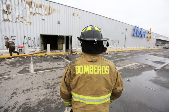 epa07937527 Firemen work at a supermarket burnt and looted during the demonstrations against the increasing of Metro fares and the social inequality in Santiago, Chile, 20 October 2019. Chile&#039;s G ...