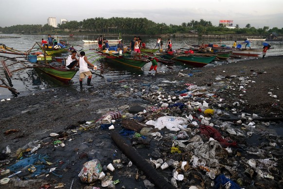 epa05112137 Filipino fishermen unload their fish catch on a coastline filled with rubbish, at a fishing village in Paranaque city, south of Manila, Philippines, 20 January 2016. According to a new rep ...