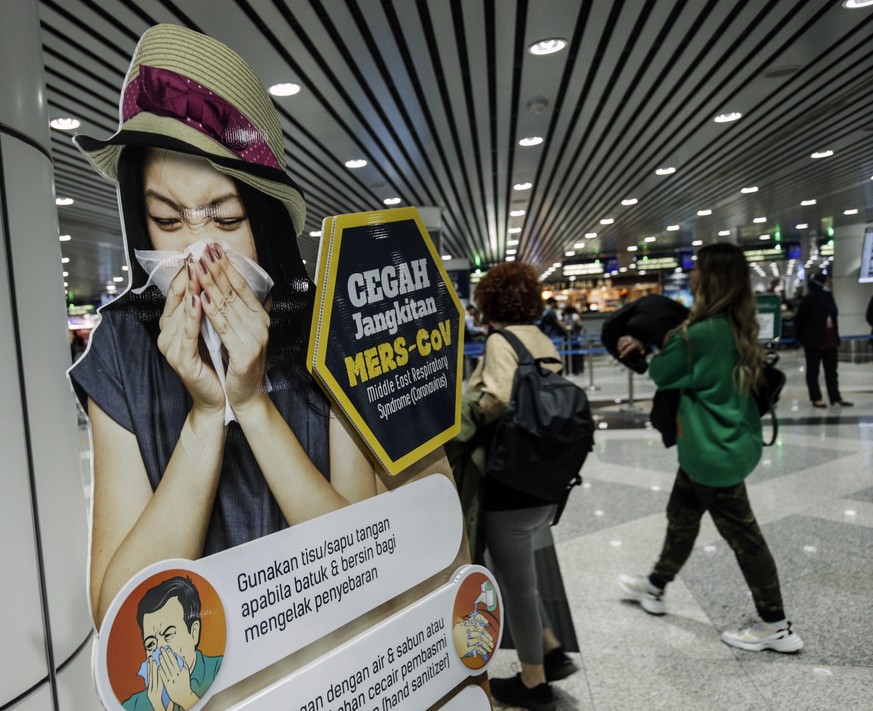 epa08146766 Passengers walk past a poster alerting on coronavirus screening ahead upon their arrival at the Kuala Lumpur International Airport (KLIA) in Sepang, outside Kuala Lumpur, Malaysia, 21 Janu ...