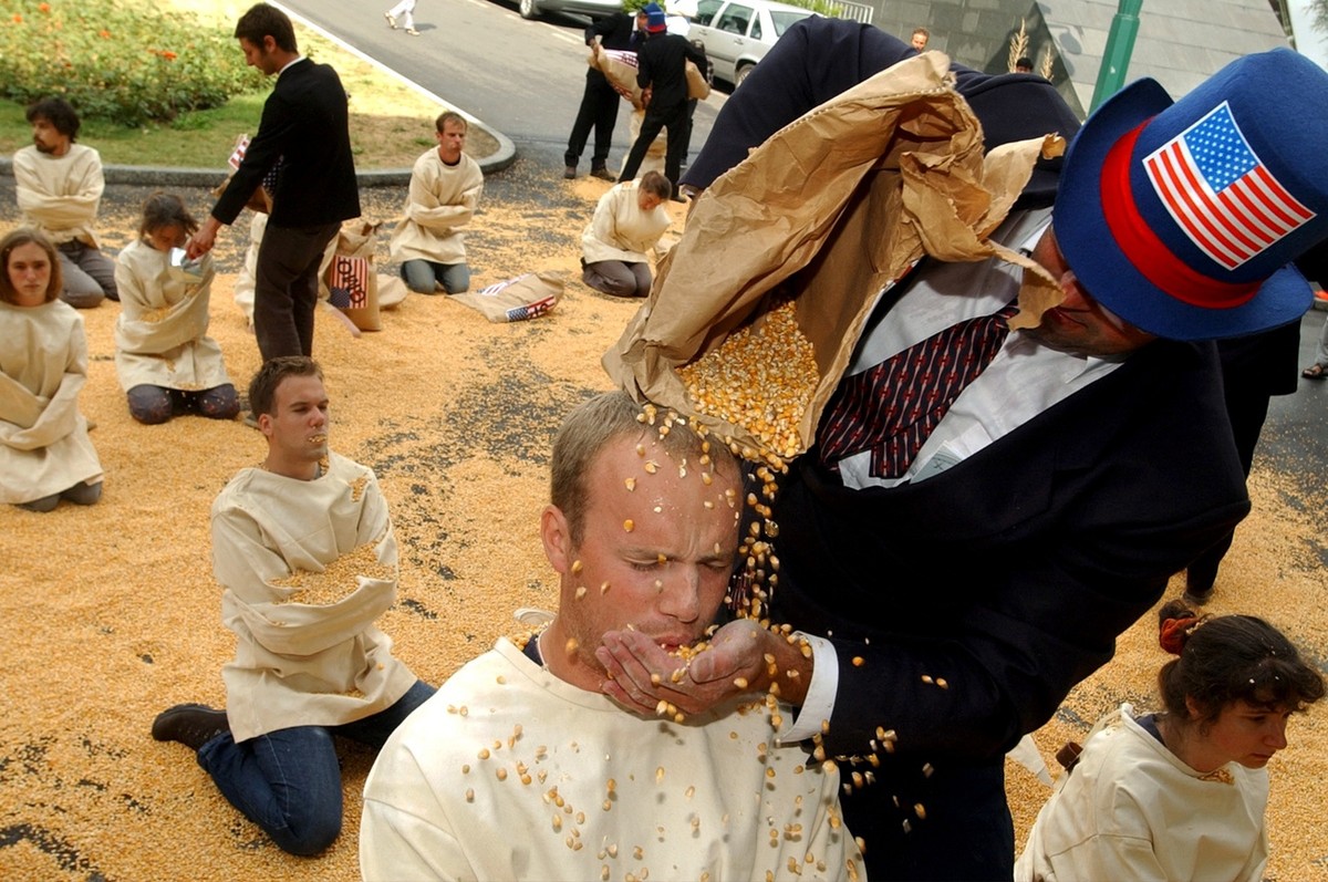 Greenpeace activists dressed as Uncle Sams pour grains of maize onto "consumers" in straitjackets in front of the World Trade Organisation, WTO, headquarters in Geneva, Switzerland, Monday,  ...