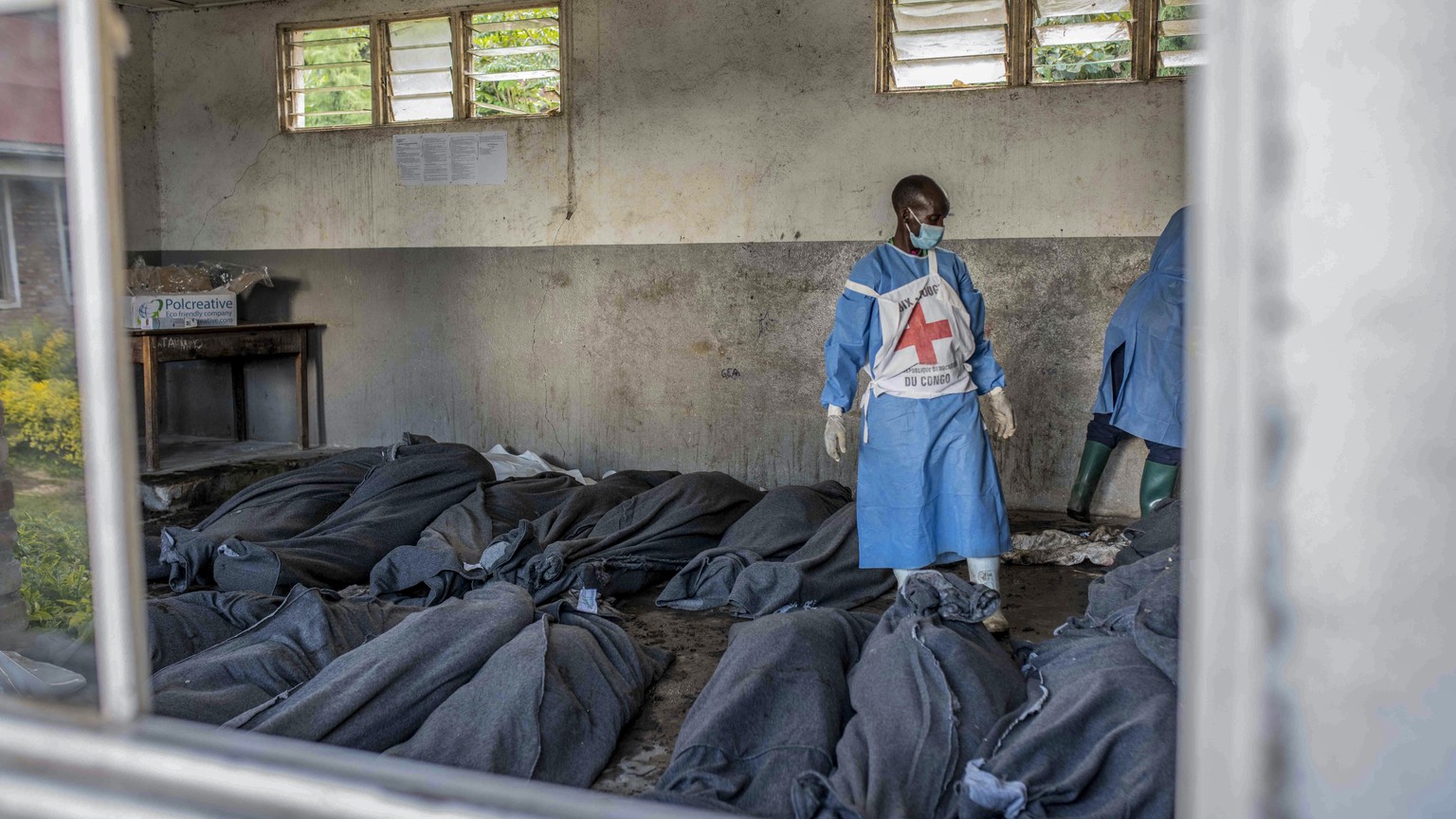 A Red Cross worker stands next to bodies at a makeshift morgue at a primary school in Bushushu, South Kivu province, Congo, Saturday, May 6, 2023. The death toll from flash floods and landslides in ea ...