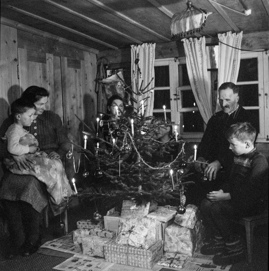 Eine Familie sitzt um den von Geschenken umgebenen Christbaum und feiert Weihnachten in der Stube ihres Wohnhauses in Ablaendschen, Kanton Bern. Aufgenommen im Dezember 1951. (KEYSTONE/PHOTOPRESS-ARCH ...