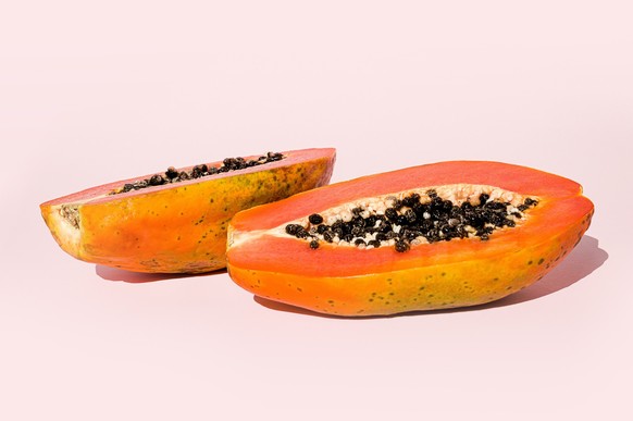 Fresh papaya exotic tropical fruit on pink background and wooden cut board. Sun day light illumination. Minimalistic summer flat lay wallpaper. Creative food concept. Copy space template.