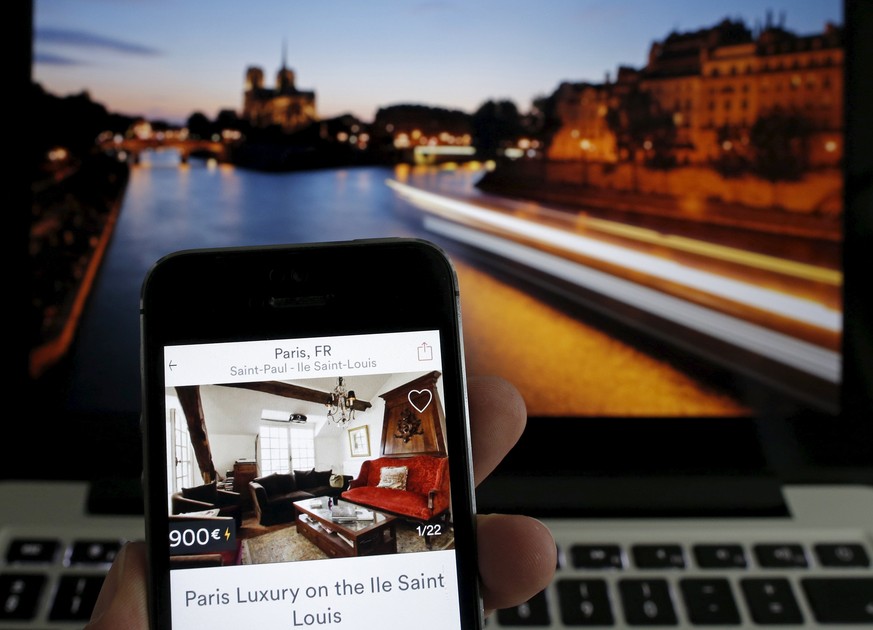An illustration picture shows the Paris apartment offer by American actress Judith Freiha on the Airbnb web page displayed on a smatphone in front of a general view of the Ile Saint-Louis on the Seine ...