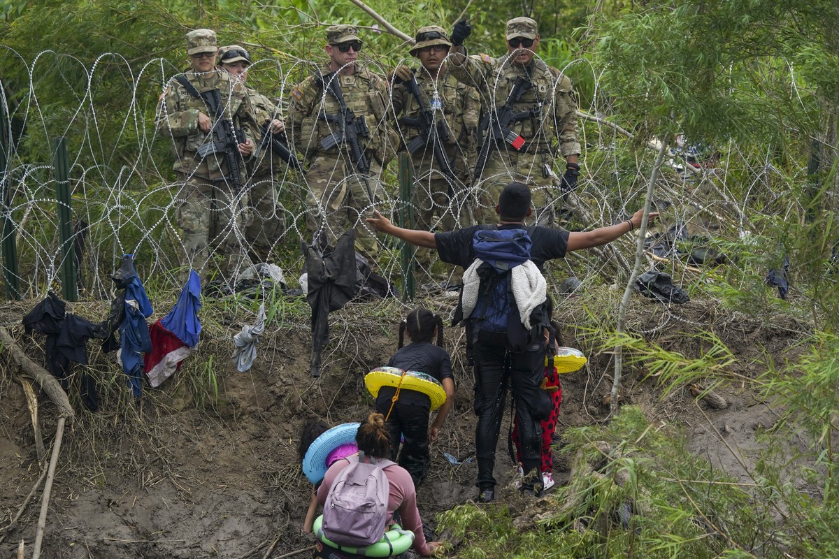 Un migrant sur le sol mexicain fait un geste vers les gardes nationaux du Texas, derrière des barbelés.