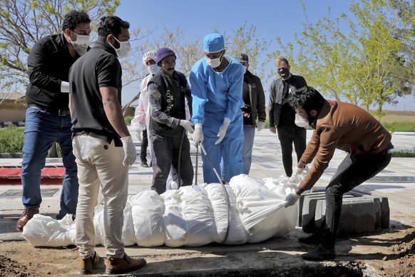 People wearing protective clothings, masks and gloves, attend the funeral of a victim who died after being infected with the new coronavirus, at a cemetery just outside Tehran, Iran, Monday, March 30, ...