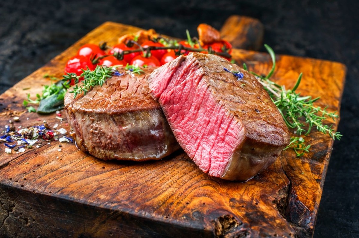 Frisiertes, trockenes Rinderfilet Medaillon, natürliches Steak mit Tomaten und Kräutern, Nahaufnahme auf einem Holzbrett