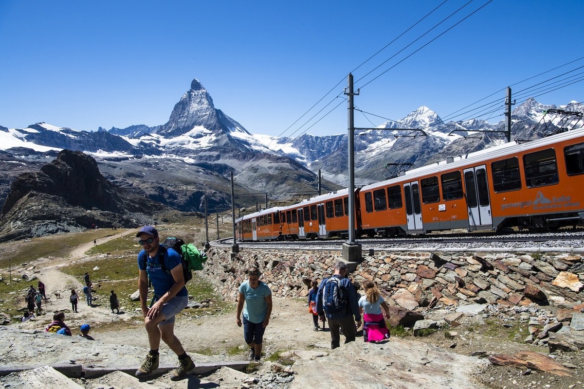 Des touristes marchent dans la montagne depuis le Gornergrat en face du Cervin a cote du train du chemin de fer du Gornergrat pendant la crise du Coronavirus (Covid-19) a l'occasion des vacances  ...