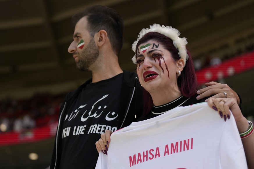 An Iran supporter, right, cries as she holds a shirt that reads &#039;Mahsa Amini&#039; an Iranian woman who died while in police custody in Iran, prior to the start of the World Cup group B soccer ma ...