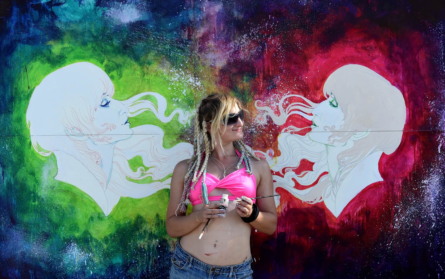 In this Aug. 25, 2014 photo, a woman poses in front of a paining during Burning Man in the Black Rock Desert of Gerlach, Nev. Organizers call Burning Man the largest outdoor arts festival in North Ame ...