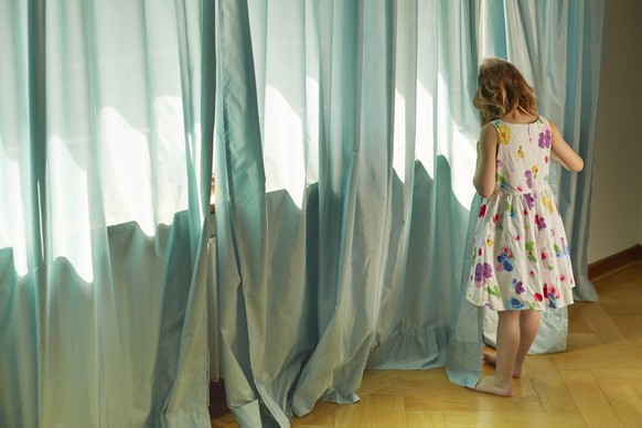 [Symbolic Image, Posed Picture] Girl standing on a window, hiding her face with a curtain. - Girl, Child, Hide, defenseless, unprotected, child abuse, (Photo by KEYSTONE/Christof Schuerpf) 

[Gestellt ...