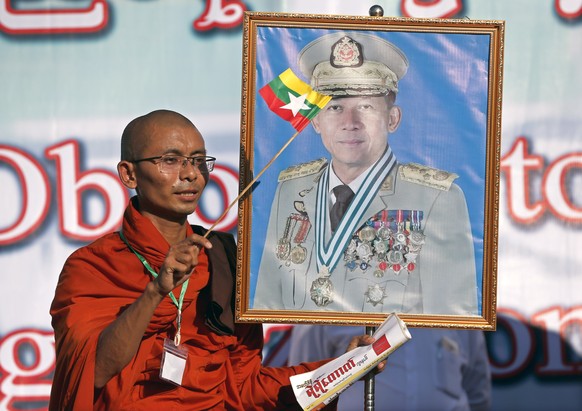 epaselect epa07092521 A Myanmar nationalist Buddhist monk waves the national flag as he holds a portrait of Myanmar military commander in chief Senior General Min Aung Hlaing during a rally to show su ...