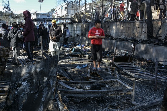 Migrants stand on a burned container home in Moria refugee camp on the northeastern Aegean island of Lesbos, Greece, Monday, March 16, 2020. The Fire Service said a migrant, who was not further identi ...