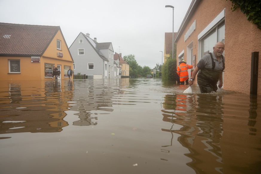 02.06.2024, Bayern, Wertingen: In einer �berfluteten Stra�e schleppt ein Mann Sands�cke. Nach dem Starkregen der letzten Tage kam es zu schweren �berschwemmungen in der Region. Foto: Stefan Puchner/dp ...