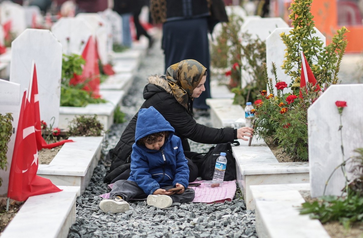 Ein Kind spielt, während eine Frau am ersten Jahrestag des verheerenden Erdbebens, das die Türkei und Syrien erschütterte, auf dem Hatay-Erdbebenfriedhof in Hatay, Türkei, trauert, 06. Februar 2024. I ...