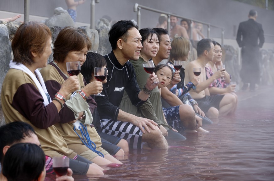 epa11732352 People hold glasses filled with 2024 Beaujolais Nouveau wine, or grape juice for children, as they bathe in a red-colored hot water bath on the day of the Beaujolais Nouveau official relea ...