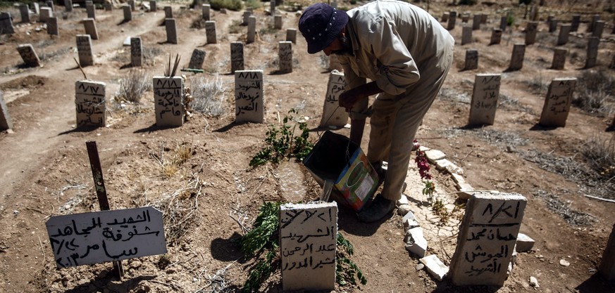 epa05507078 A picture made available on 22 August 2016 showing Abo Ezzo, a worker in the cemetery of Douma, drops some water and put a green branch on the tombs of Abd al-Rahman al-Moudawer, a volunte ...