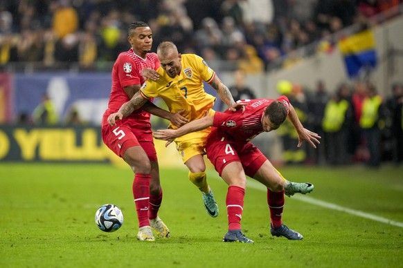 Romania&#039;s Denis Alibec is tackled by Switzerland&#039;s Manuel Akanji, left, and Switzerland&#039;s Nico Elvedi during the Euro 2024, group I, qualifying soccer match between Romania and Switzerl ...