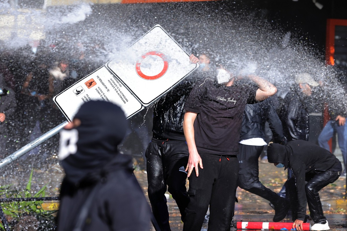 Hooded protesters use a road sign as a shield against a police water cannon during clashes in Tirana, Albania, Wednesday, Oct. 14, 2026, joining a demonstration organized by the Flamingo protest movem ...