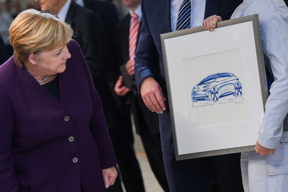 epa07971585 German Chancellor Angela Merkel (L) looks at a graphic representation of the new electric car Volkswagen ID.3, hold by worker Lea Fuchs (R) at the Volkswagen ID.3 car assembly line during  ...