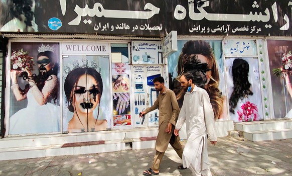 epa09421982 Afghan men walk past the billboard of a beauty saloon with defaced posters of models in Kabul, Afghanistan, 20 August 2021. The Afghan interim council, formed to assist in the power transf ...