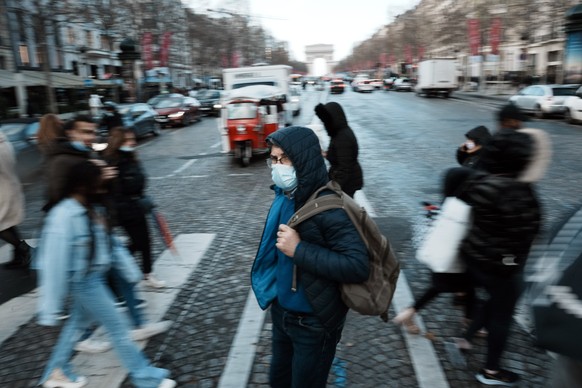 A man wearing a face mask to prevent the spread of the COVID-19, crosses the Champs Elysees avenue, in Paris, Tuesday, Dec. 28, 2021. The French government has announced new COVID-19 measures in an ef ...