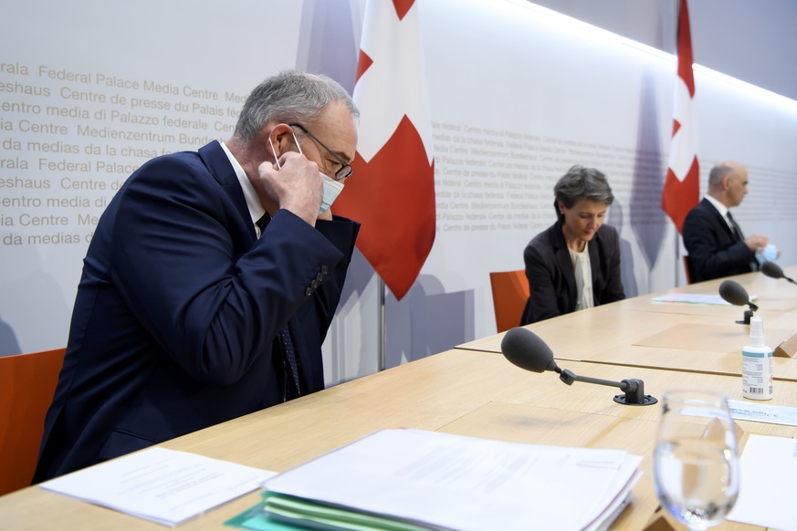 Bundesrat Guy Parmelin nimmt seinem Schutzmaske ab, links, an der Seite Bundespraesidentin Simonetta Sommaruga, Mitte, und Bundesrat Alain Berset, rechts, an einer Medienkonferenz, am Freitag, 18. Dez ...