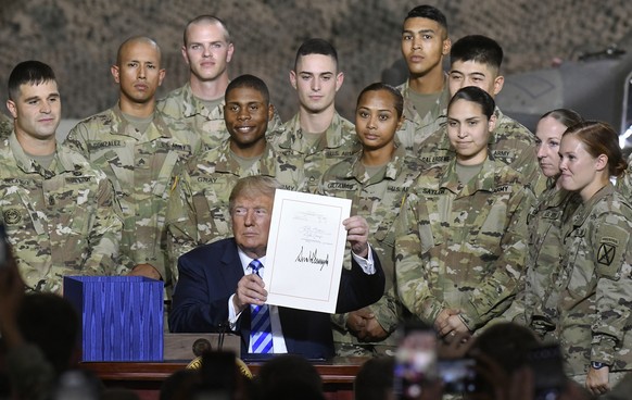 President Donald Trump holds up the $716 billion defense policy bill named for Sen. John McCain that he signed during a ceremony Monday, Aug. 13, 2018, in Fort Drum, N.Y. (AP Photo/Hans Pennink)