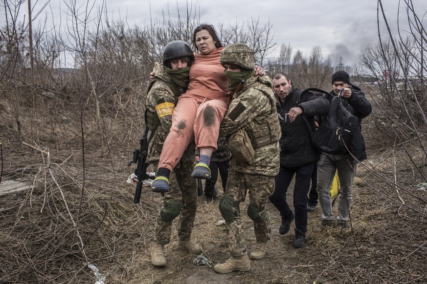 A woman carried by Ukrainian soldiers crosses an improvised path while fleeing the town of Irpin, Ukraine, Sunday, March 6, 2022. In Irpin, near Kyiv, a sea of people on foot and even in wheelbarrows  ...