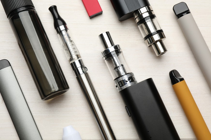 Different electronic cigarettes on white wooden table, flat lay.  Alternative to smoking