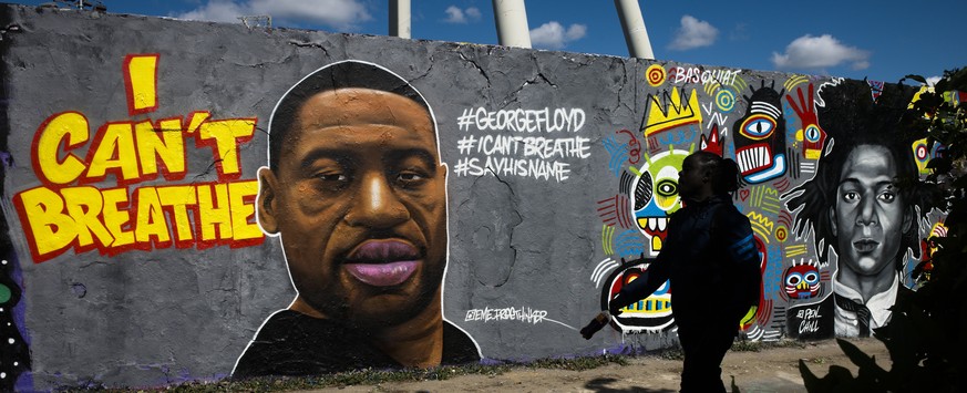 A man walk in front of a graffiti by artist 'EME Freethinker' that depict George Floyd is painted on a wall in the public park Mauerpark in Berlin, Germany, Saturday, May 30, 2020. Floyd die ...