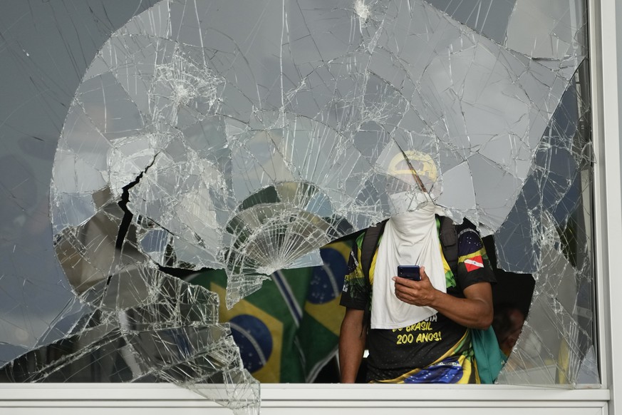 Protesters, supporters of Brazil's former president Jair Bolsonaro, pout from a shattered window after storming the Planalto Palace in Brasilia, Brazil, Sunday, January 8, 2023.  Planalto is the of ...