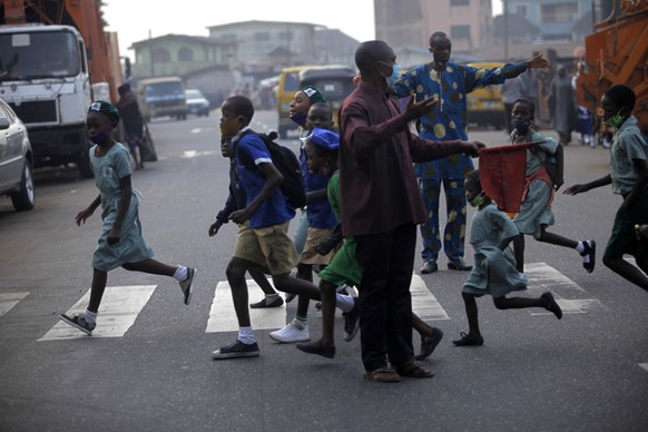 epa08958253 A man waves a red flag to direct traffic on a zebra crossing sign as school children cross the road in front of the Dairy Farm primary school in Agege district of Lagos,Nigeria, 22 January ...