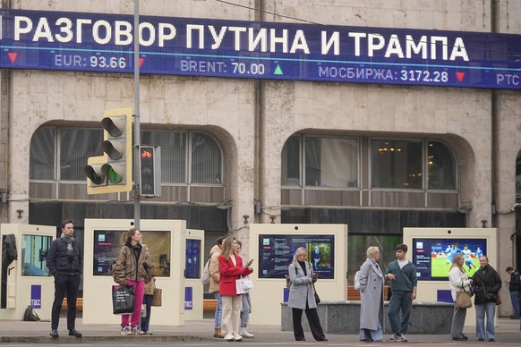 People wait at a traffic light to cross a street with a news ticker in the background reporting on possible phone call between Russian President Vladimir Putin and US President Donald Trump, on the fa ...