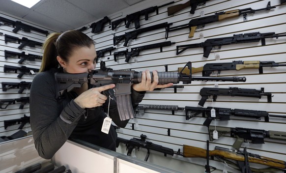 Gun shop owner Tiffany Teasdale-Causer points a Ruger AR-15 semi-automatic rifle, the same model, though in gray rather than black, used by the shooter in a Texas church massacre two days earlier, as  ...