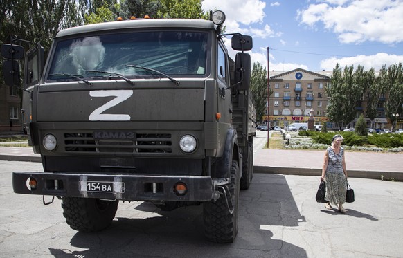 epa10072567 A picture taken during a visit to Melitopol organized by the Russian military shows a woman walking past a Russian military truck in downtown Melitopol, Zaporizhia region, southeastern Ukr ...