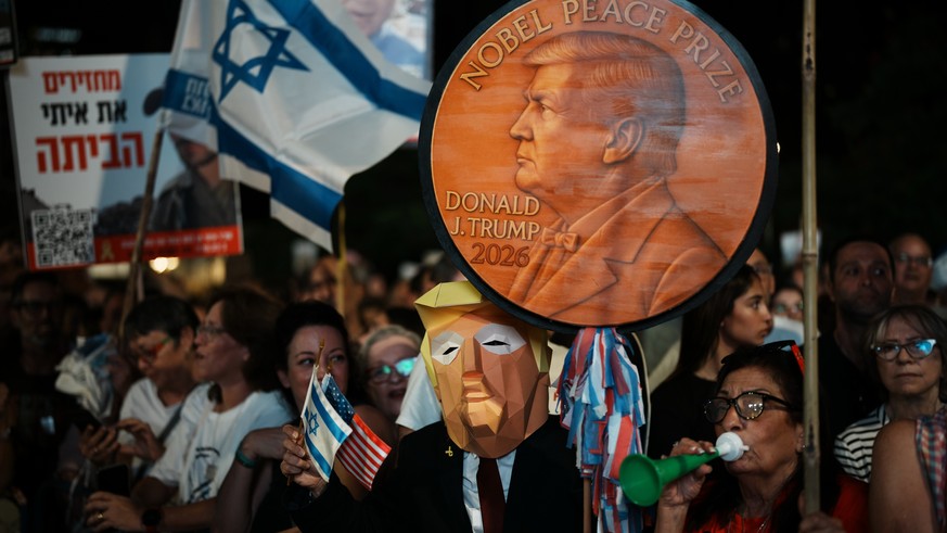 A man wearing a mask resembling U.S. President Donald Trump holds a sign designed like a Nobel Peace Prize medal during a rally in support of hostages held by Hamas, at Hostages Square in Tel Aviv, Is ...