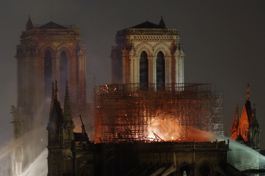 Firefighters tackle the blaze as flames and smoke rise from Notre Dame cathedral as it burns in Paris, Monday, April 15, 2019. Massive plumes of yellow brown smoke is filling the air above Notre Dame ...