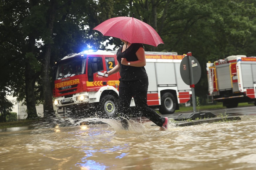 A woman walks past fire trucks at a flooded street with an umbrella Duesseldorf, Germany, Wednesday, July 14, 2021. Storms caused widespread flooding across central Germany overnight, with authorities ...