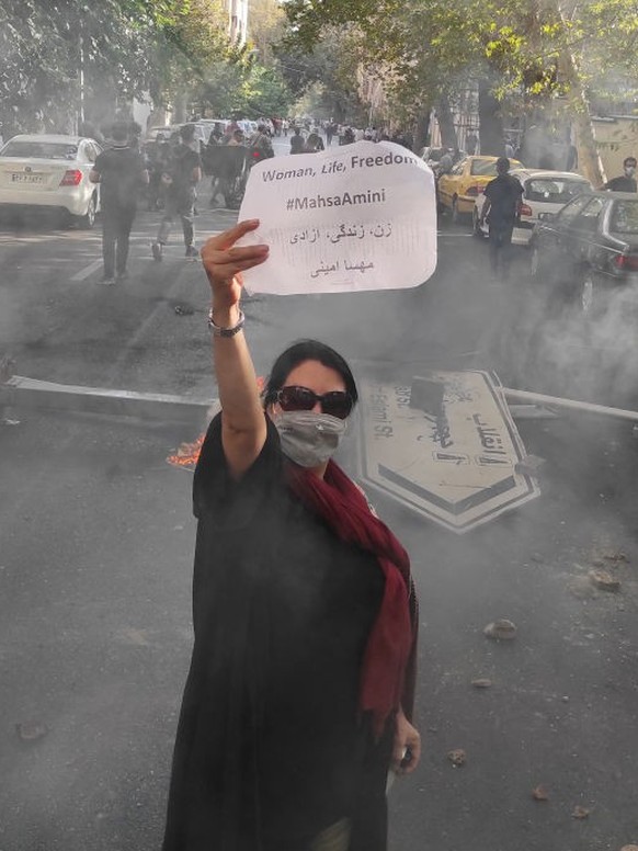 TEHRAN, IRAN - OCTOBER 01: (EDITORS NOTE: Image taken with mobile phone camera.) A protester holds up a note reading &quot;Woman, Life, Freedom, #MahsaAmini&quot; while marching down a street on Octob ...