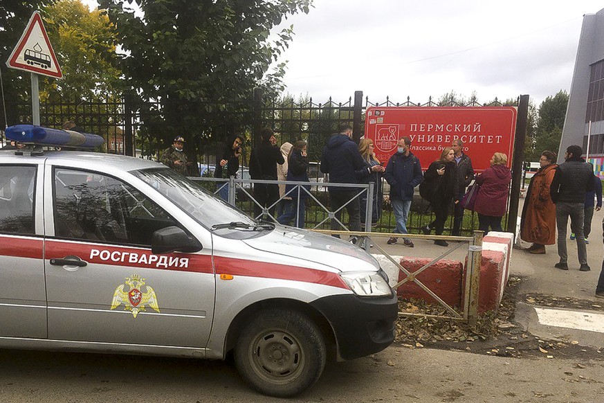 People stand behind the fence near the Perm State University with the a Posguardia (National Guardia) on the left, in Perm, Russia, Monday, Sept. 20, 2021. A gunman opened fire in a university in the  ...