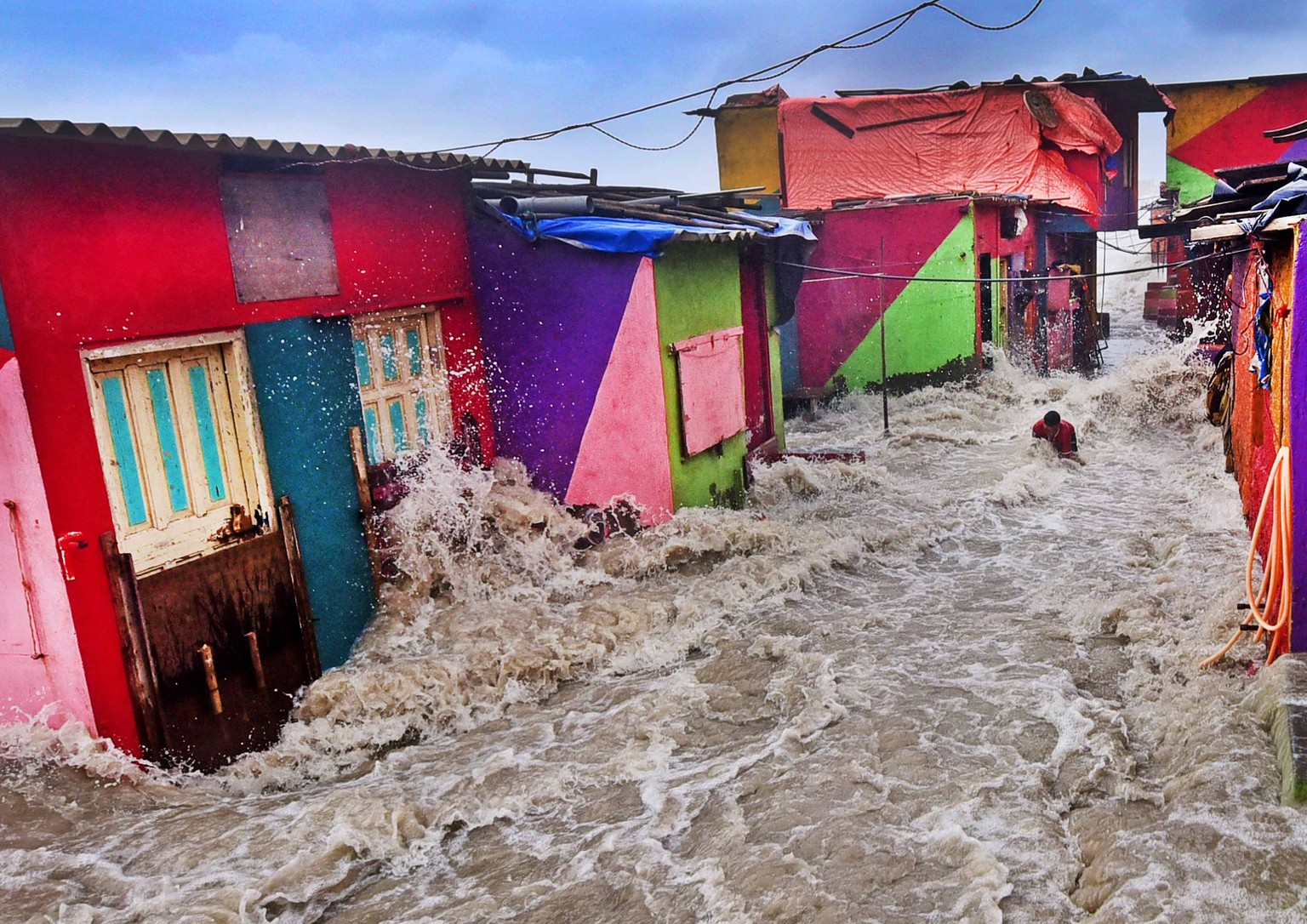 Mumbai: A high tide wave hits a man standing outside his house as the seawater enters the shanty town near the shore, at Bandra bandstand in Mumbai on Monday, Aug 13, 2018.