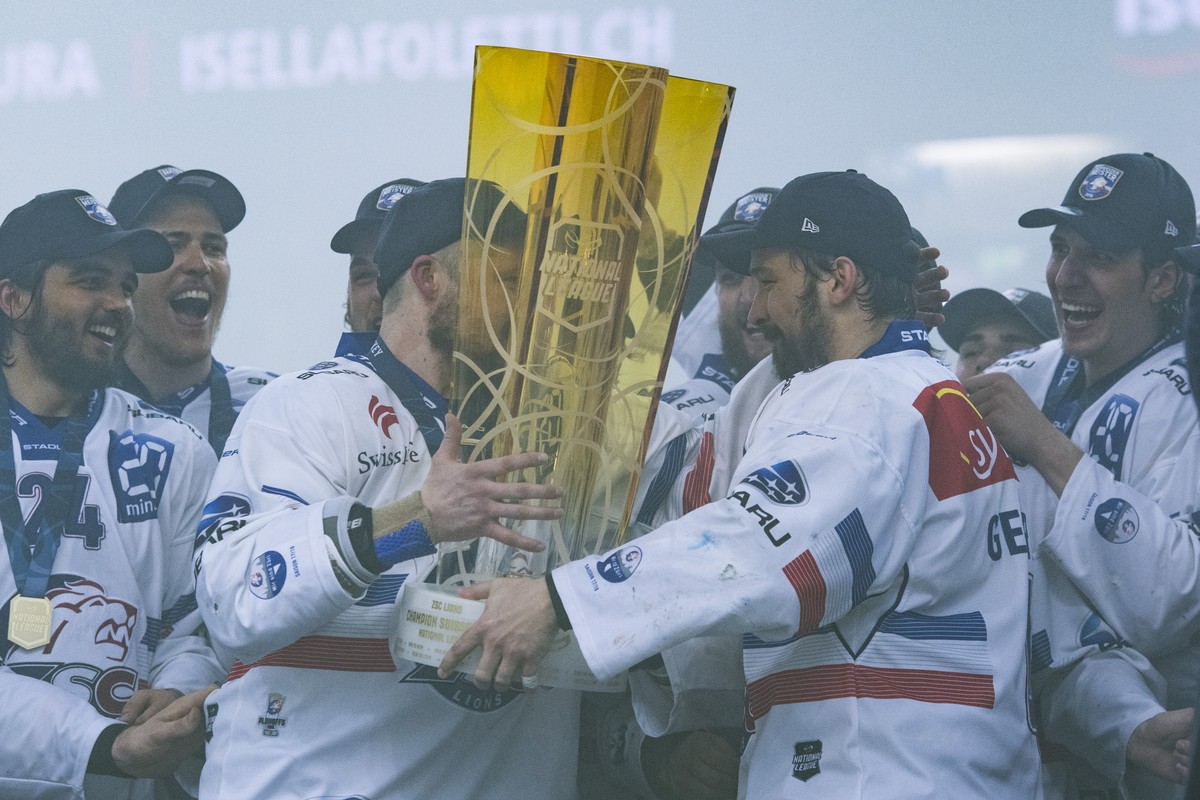 Zurich's player Patrick Geering, right, gives the trophy to teammate Mathias Seger, left, after winning the Swiss championship title, during the seventh match of the playoff final of the National ...